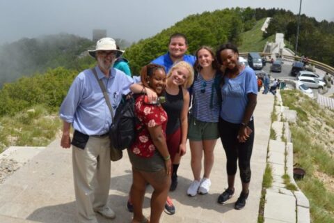 Students and a professor stand at the top of a hill overlooking the countryside