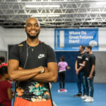 Quinton Coe smiles at the Boys and Girls Club. In the background, people are visiting with each other and a sign reads, "Where great futures start."