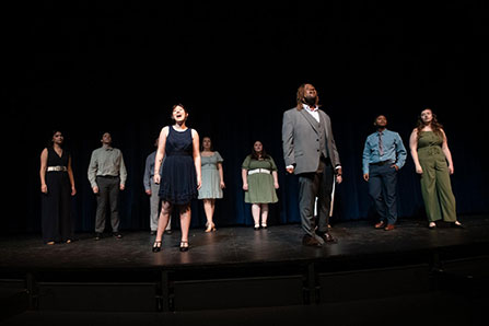 A group of students perform on a darkened stage.