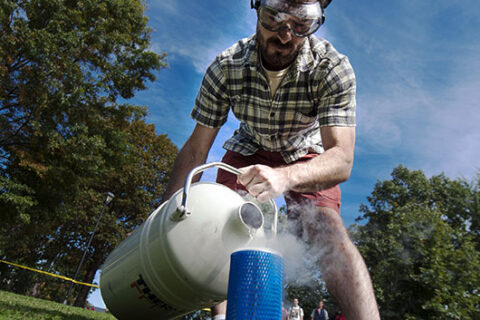 Jason Crumpton conducting a chemistry experiment outdoors by pouring a liquid into a blue tube