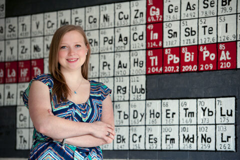 Karen Butler '14 standing in front the periodic table of elements