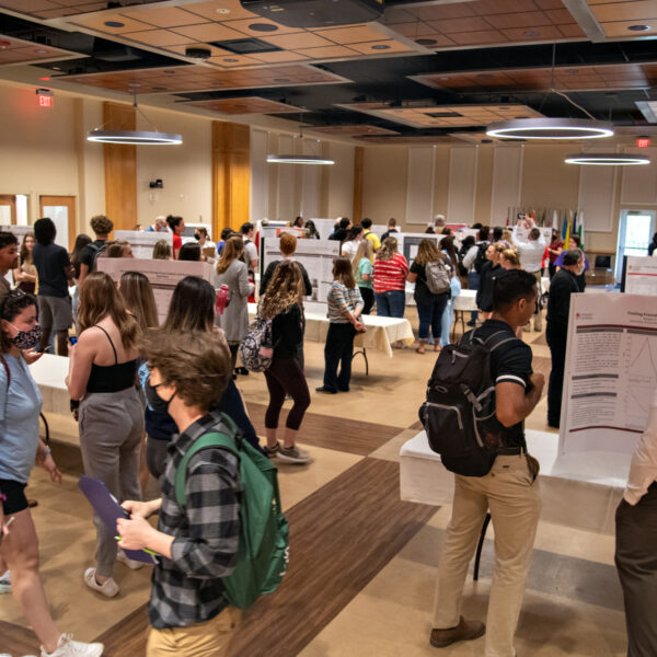 A poster presentation with lots of attendees walking around inside a large indoor space