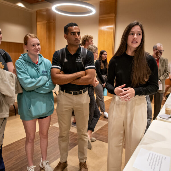 A group of three students listens to a poster presentation by another student