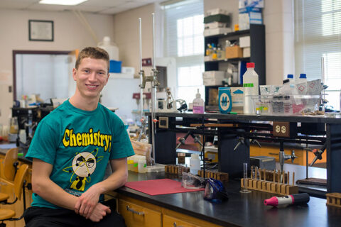 A student sitting on a tool in front of a lab table in a chemistry lab