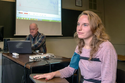 A student is sitting in a chair while her professor is giving her a polygraph test