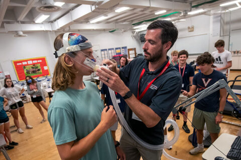 A professor is helping a student put on an oxygen measuring device in a lab