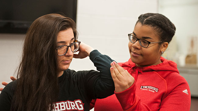A student helps another student stretch her shoulder.