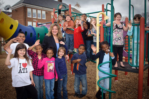 A woman standing in a playground, surrounded by children