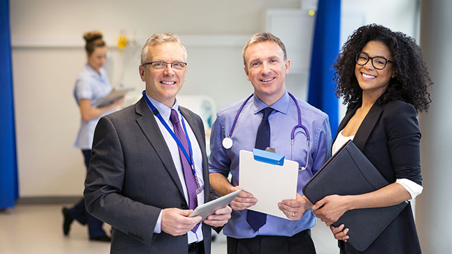 A doctor and two administrators standing in a hospital, looking at the camera