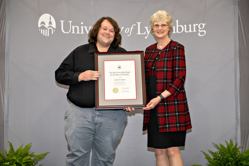 White man with long hair and white woman pose for a photo with framed certificate