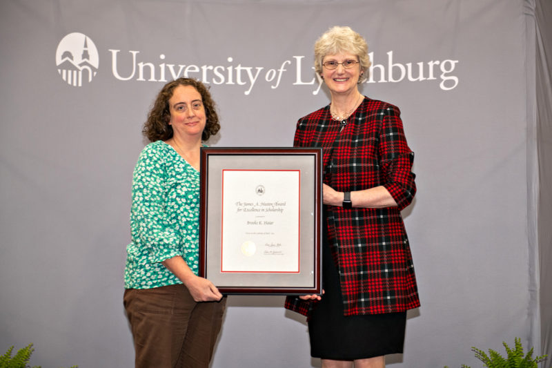 Two white women posing for a photo holding a framed certificate between them