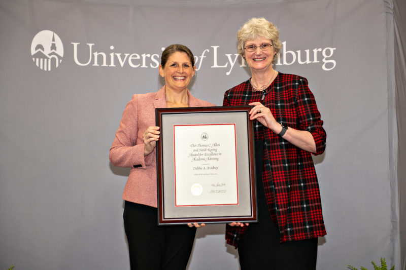 Two white women posing for a photo with a framed certificate