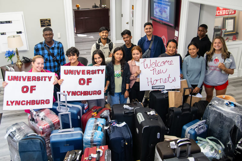 A group of students with suitcases holding welcome signs 