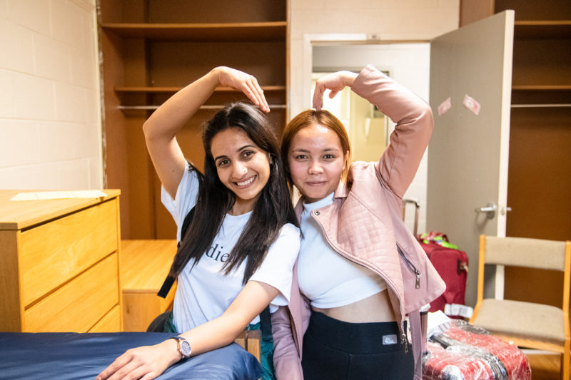 Two female students make a joint heart with their arms in their dorm room