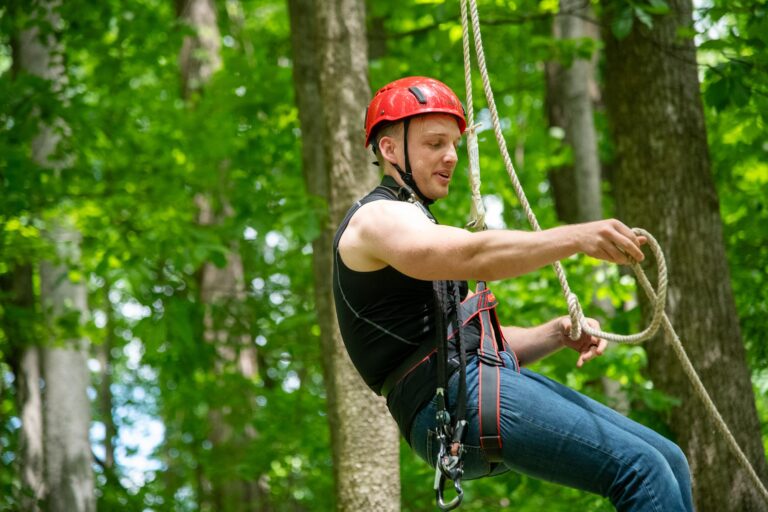 A man wearing a helmet and harness, suspended from a high ropes course.