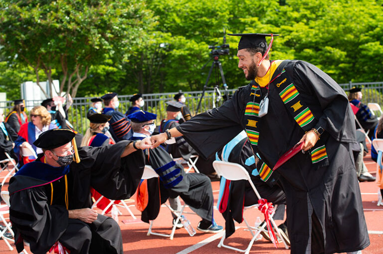Claudio Otero fist bumps a professor at commencement