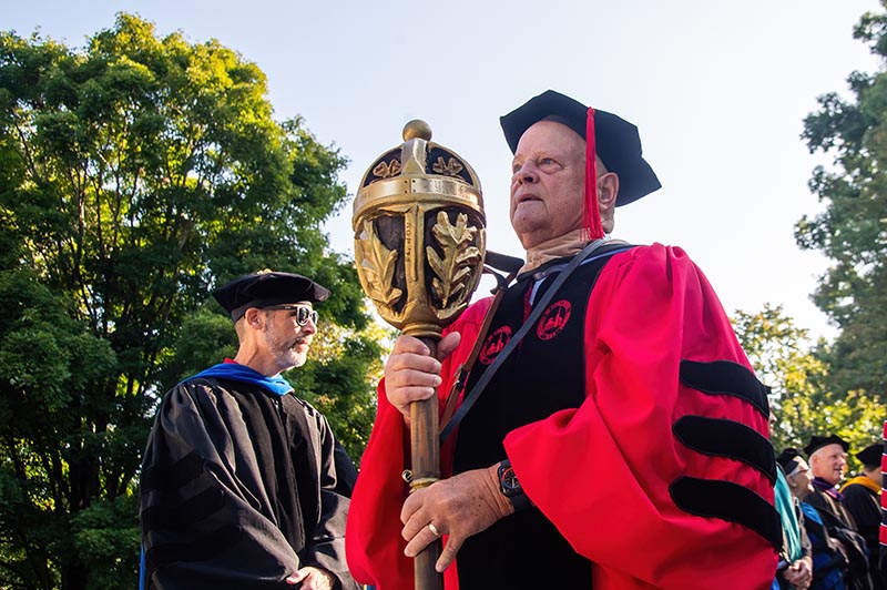Frank Whitehouse, professor of marketing and chair of the marketing department, carries the University of Lynchburg Mace at the head of the 2024 Convocation procession. This official symbol of academic authority is carried by the University marshal, the senior faculty member, at Convocation and all official ceremonies. The Mace was carved from a pine ceiling beam from Westover Hall, the University’s original building, which was dismantled in 1970.