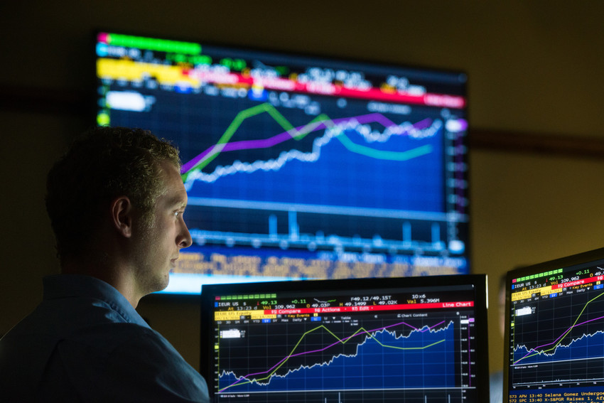 A person analyzing financial data on multiple monitors displaying stock market graphs and charts in a dimly lit room.