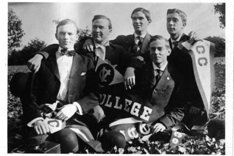 A group of male students pose holding Virginia Christian College flags.