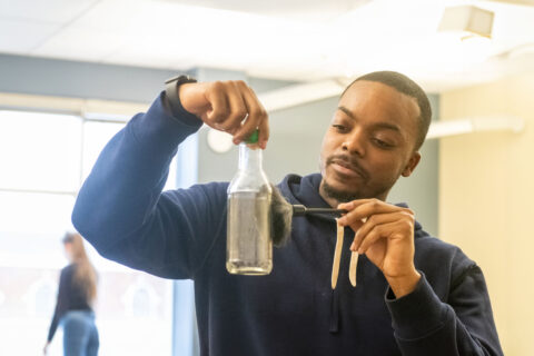A dedicated criminal forensics student at the University of Lynchburg conducting a laboratory experiment, analyzing samples in a clear glass bottle to learn scientific techniques for crime scene investigation. This image illustrates hands-on learning in forensic science education.