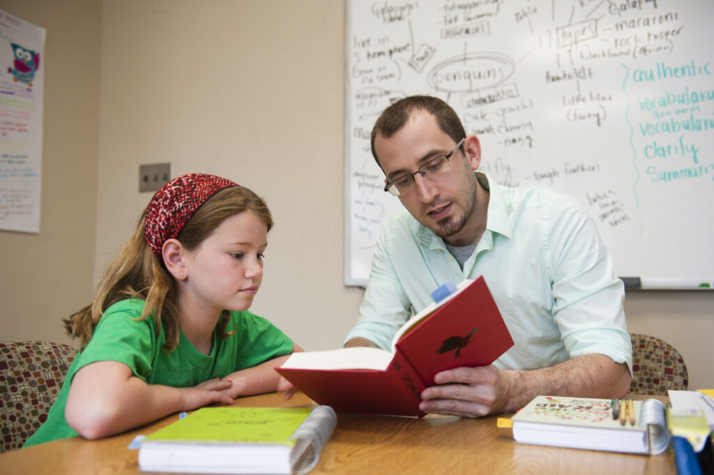 A man holds and reads from a book to a young girl at a table.