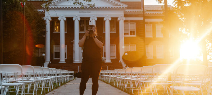 Whitney grim talks a picture at sunrise in front of Hopwood Hall