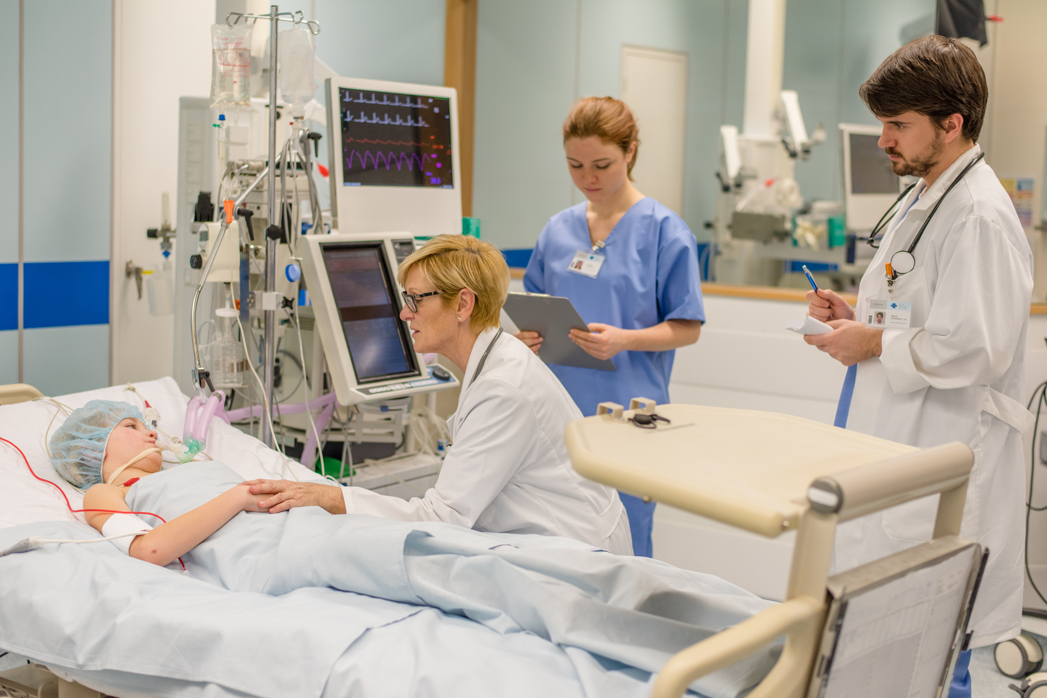 Medical providers gather around a patient lying in a hospital bed.