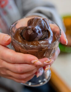A student holds up a cup of chocolate pudding and chocolate frogs