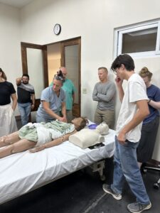 Bryn Kroto demonstrates proper CPR on a mannequin to a group of observers. 