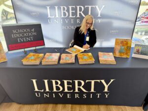 Becky Clark sits at a table signing her book. 