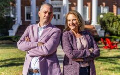 A man and a woman pose for a photo. Both are wearing light purple sports coats and both are crossing their arms over their chests.