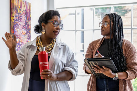 Two women talking and walking through a gallery.