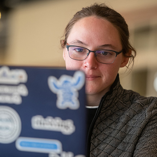 Close-up of a student wearing glasses looking at a laptop covered in stickers.