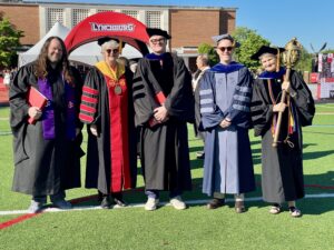 A group wearing academic regalia stands on a field smiling. 
