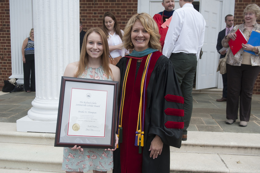 Student award recipient and faculty member pose outdoors with a framed scholarship certificate during a campus recognition event.