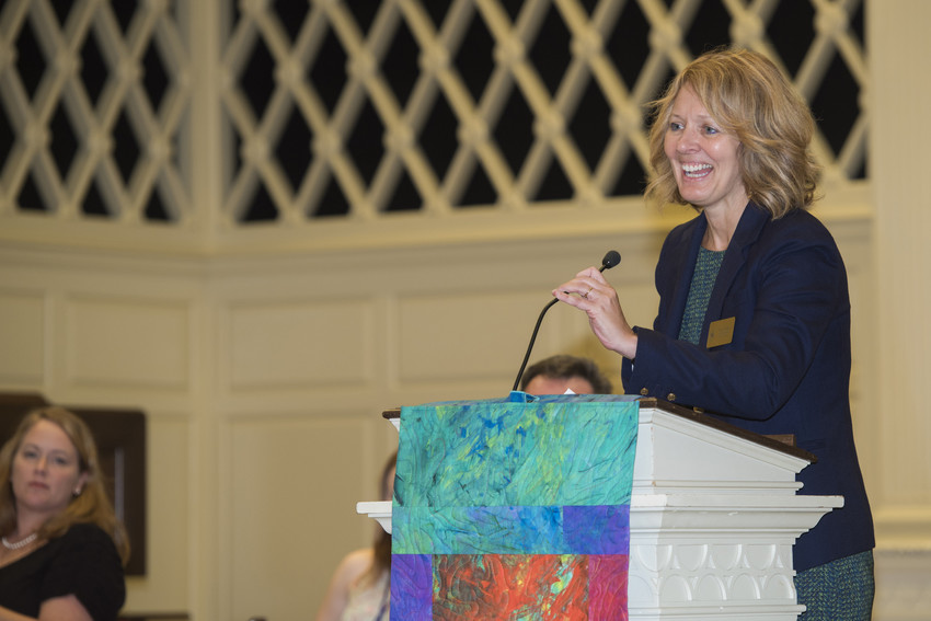 Woman smiles while speaking at a podium during a formal campus ceremony.