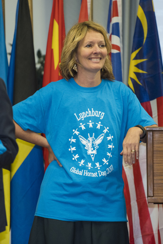 Woman in a blue Global Hornet Day 2017 shirt stands smiling in front of international flags.