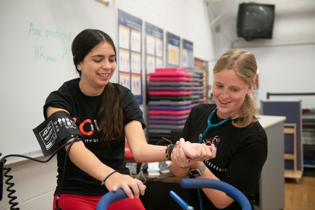 A student measures blood pressure and pulse of a student on an exercise bike.