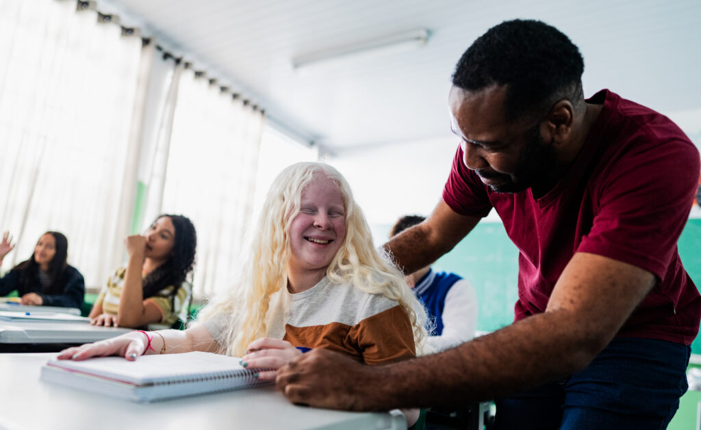 Educator provides individualized support to student with albinism in inclusive school environment, demonstrating pedagogical practices that value diversity and promote educational accessibility through personalized attention that ensures full participation of students with different physical characteristics in the learning process