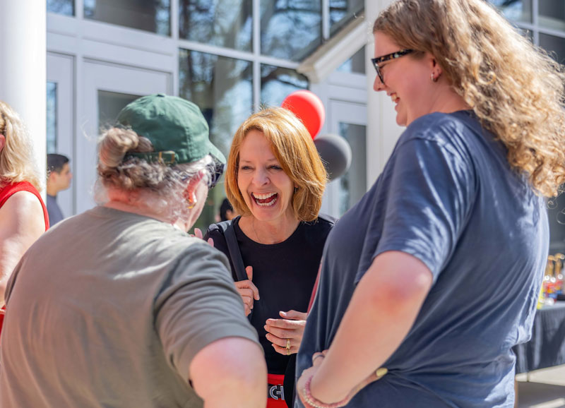 Woman laughs while talking with attendees at an outdoor campus gathering.
