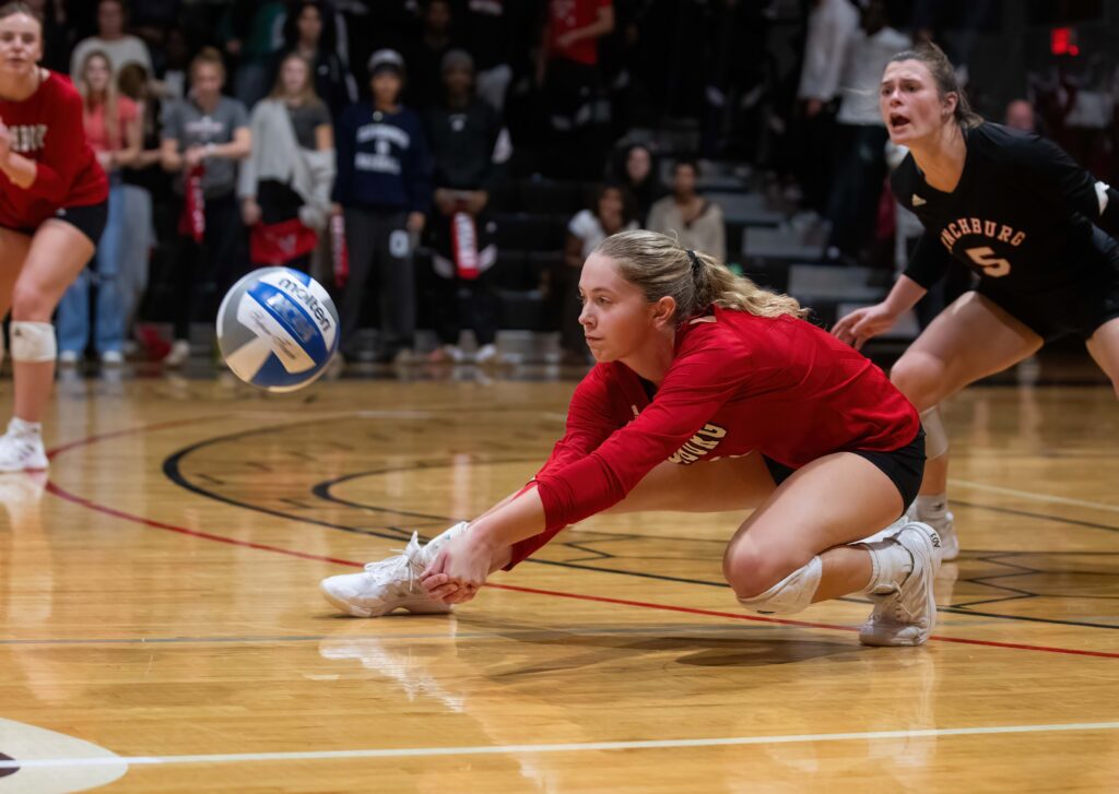 female lynchburg player dives onto gym floor to volley the ball during a match.