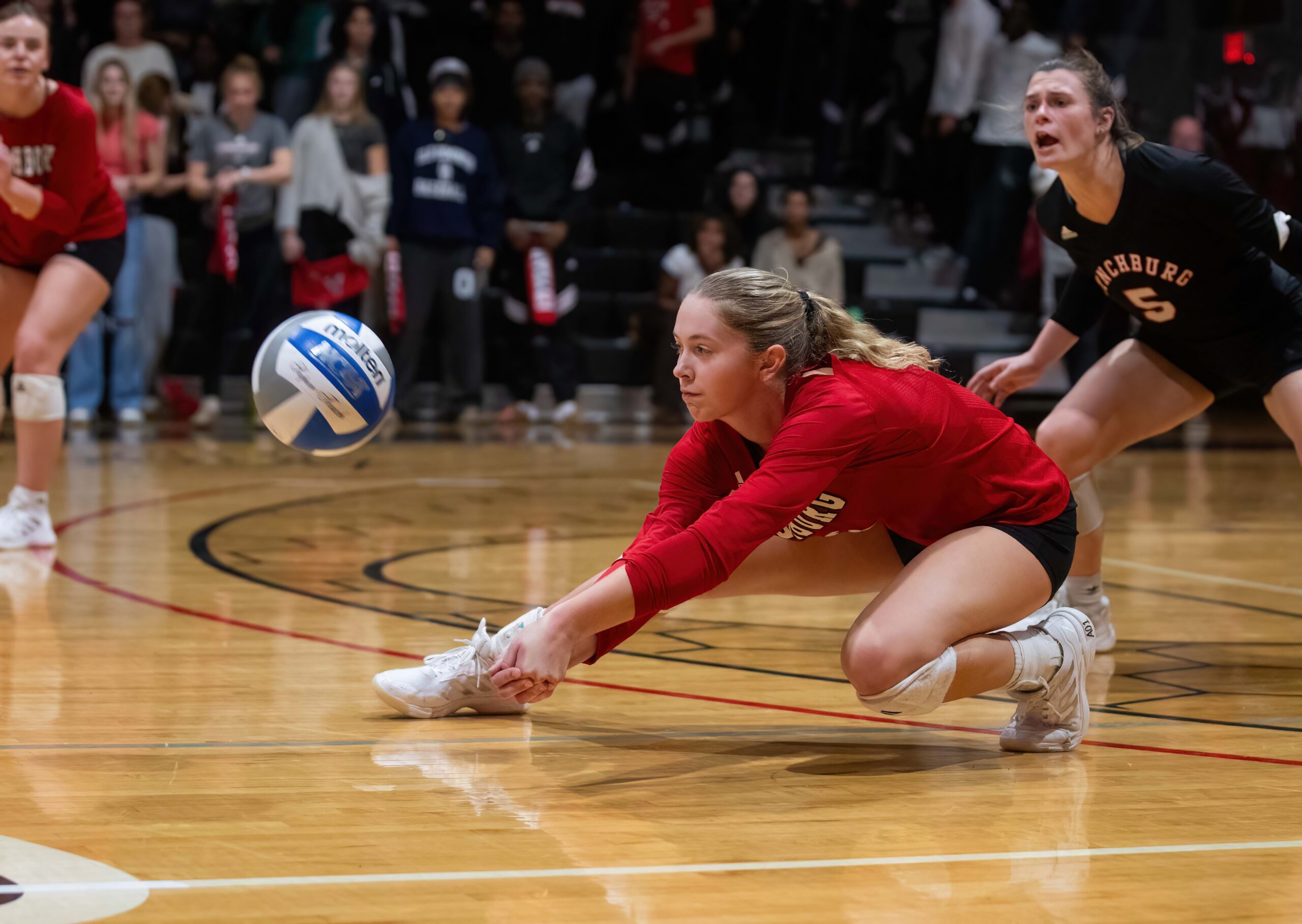 female lynchburg player dives onto gym floor to volley the ball during a match.