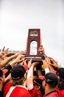 An NCAA trophy is lifted by multiple hands