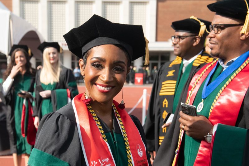 A woman of color in graduation cap and gown smiling with people in the background