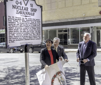Treney Tweedy holds a large banner with the Virginia seal, which she has just removed from the historical marker.