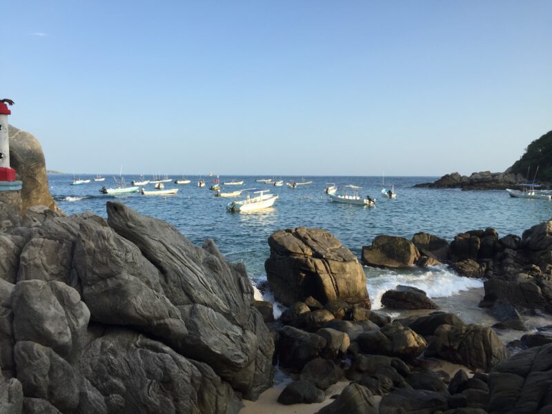 A rocky coastline with an ocean and white boats in the background
