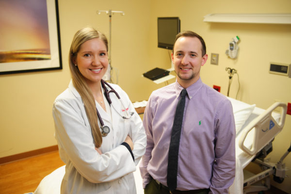 Two DMSc graduates, one in a white doctor coat and the other in business attire, in a clinic room