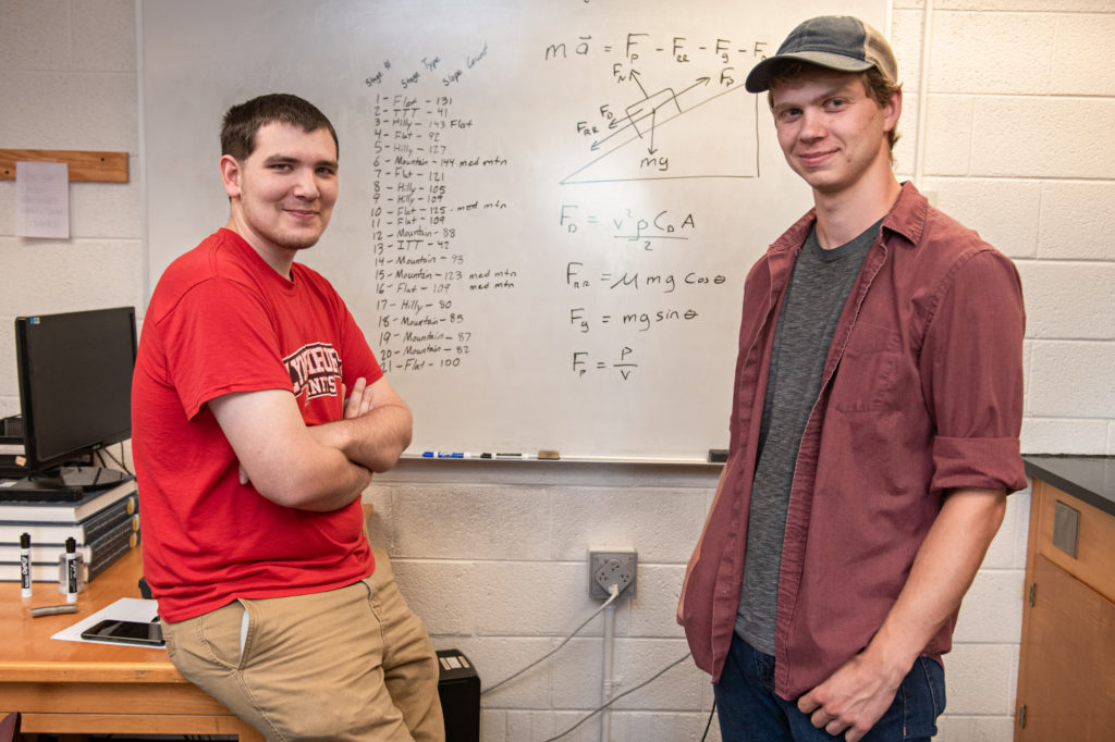 Carl Pilat and Noah Baumgartner in front of a whiteboard with equations written on it
