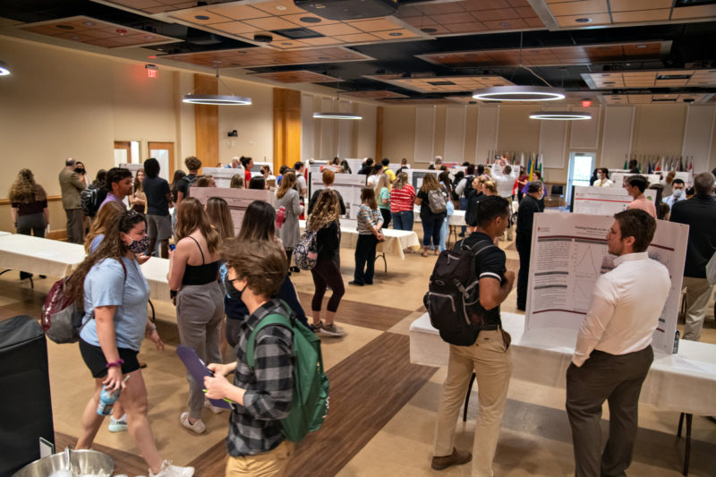 A poster presentation with lots of attendees walking around inside a large indoor space
