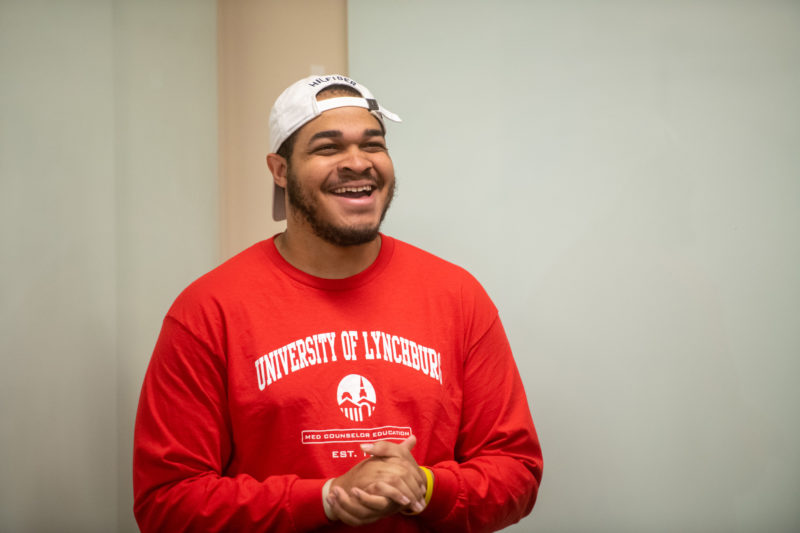 A black male student in a red sweatshirt and a white baseball cap laughing